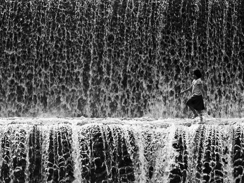 A child walking in the midst of waterfall.