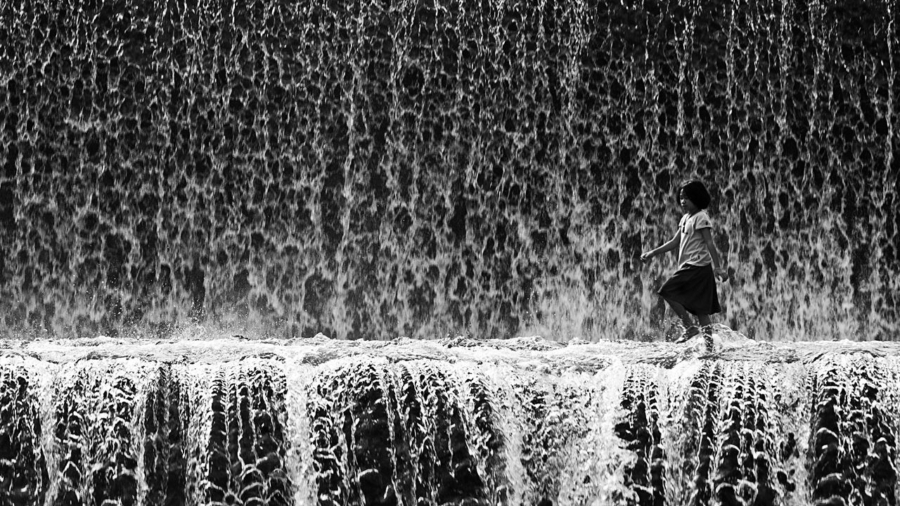 A child walking in the midst of waterfall.
